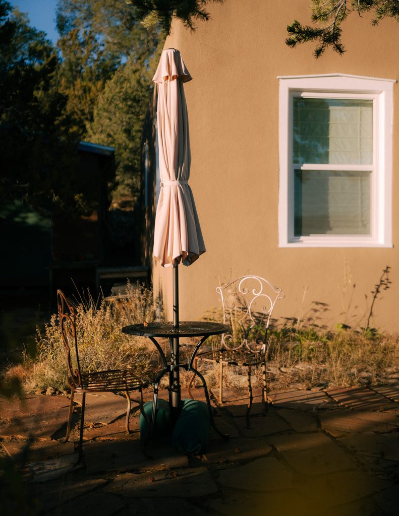 Bistro table and iron chairs against adobe wall, closed umbrella, golden hour light